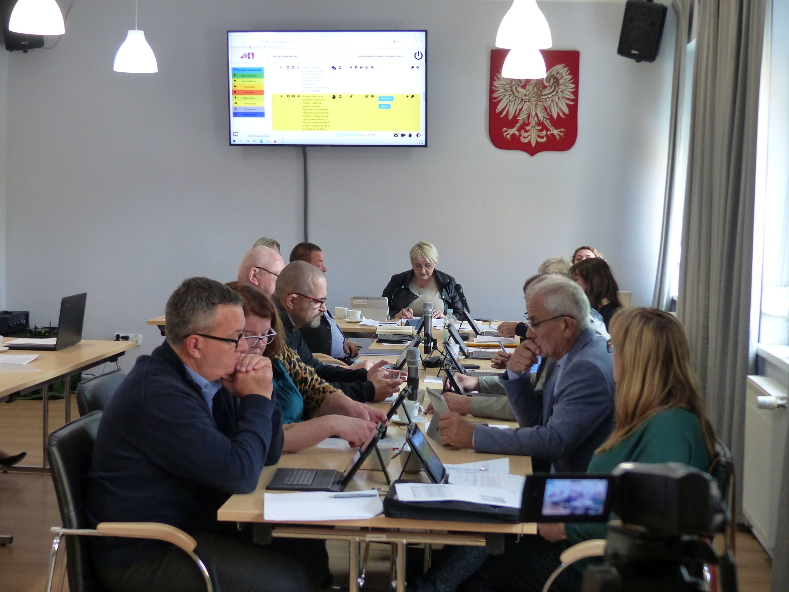 Sesja Rady Gminy Wińsko w GOK-u. Łącznie 14 radnych siedzi za stołem prezydialnym, głosują za pomocą tabletów.
