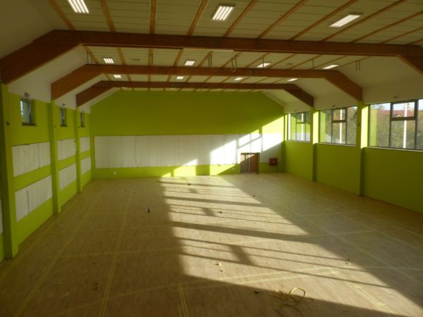 Wnętrze sali sportowe w Orzeszkowie w czasie prac. Zielone ściany, duże okna, parkiet.