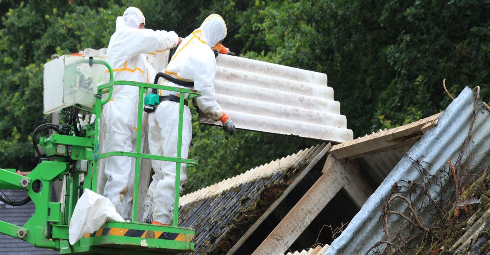 dwie osoby ściągające azbest z dachu