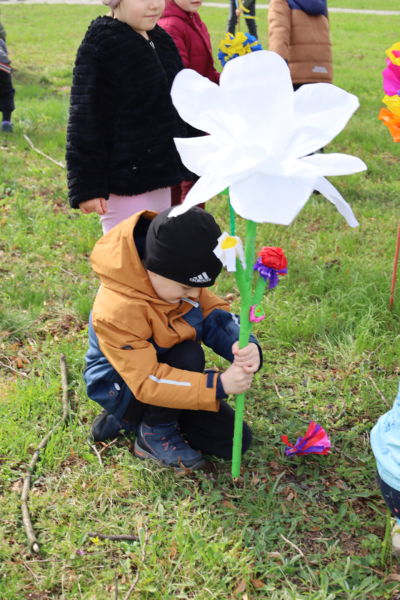 na zdjęciu chłopczyk który próbuje wbić w trawnik kwiatka z bibuły