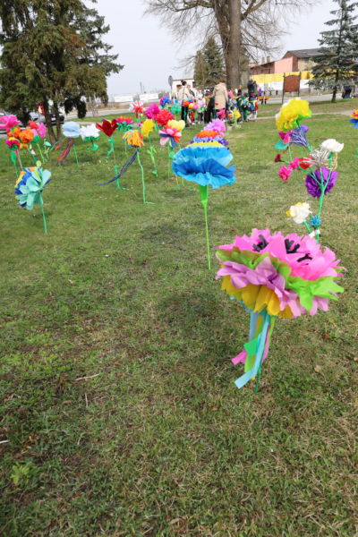 na zdjęciu kwiaty z bibuły wbite w trawnik, a na drugim planie grupka dzieci